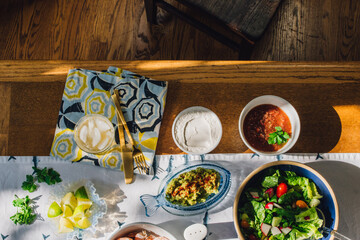 Sticker - summer Seafood supper table spread to make fish tacos, prawns, guacamole, sour cream, salad, lime, tortilla, salsa on blue and white fish tablecloth in the sun