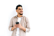 © Kateryna - Positive attractive indian or arabian guy, holding smartphone in hand, chatting online, browsing internet, looking to the side, thinking, dreaming, standing on isolated white background, smiling