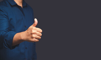 Businessman in a blue shirt shows thumbs up while standing on gray background in the office