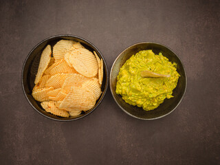 Wall Mural - A bowl with fresh guacamole and potato chips on a plate over vintage background