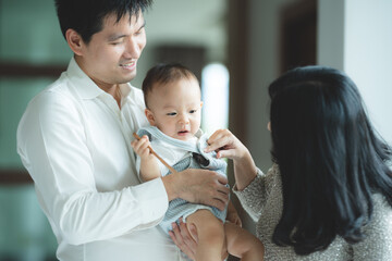 young Asian family are happy together at home by life insurance concept, child baby and mother and father having fun and smile with love, childhood living in cozy lifestyle with dad and mom