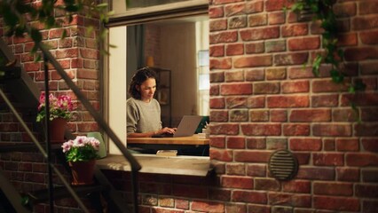 Fototapete - Hispanic Woman Using Laptop Computer, Sitting in Living Room im Her Apartment. Professional Female Working Remotely Online, Planning, Brainstorming New Project. Shot Into the Window From Outside.