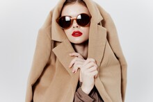 Conceptual Catalog Photography. A Girl With Glasses And A Coat On Her Head Poses On A White Background