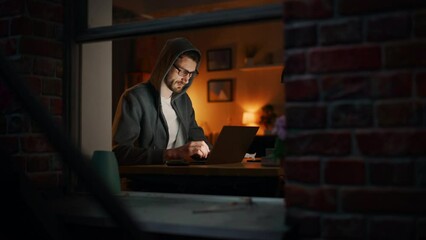 Aufkleber - Professional Male Programmer Writing Code for New Project while Working Remotely on Laptop From Home Office. Freelance Software Engineer Designs App From his Apartment. View From Outdoors into Window.