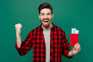 Poster - Traveler tourist man he in red shirt hold passport boarding tickets do winner gesture isolated on plain dark green background. Passenger travel abroad on weekends getaway. Air flight journey concept.