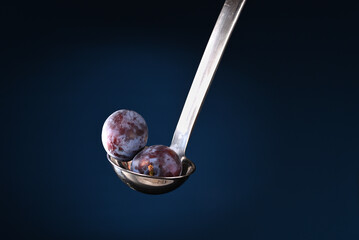 Plums in ladle on the dark blue background.