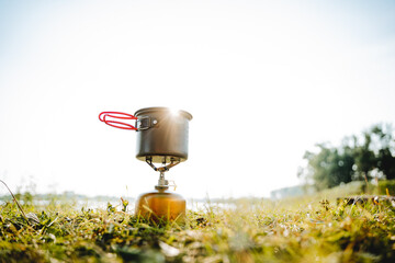 Poster - Tourist dishes stand on the grass against the background of sunset in the rays of sunlight, the pot stands on a gas burner, trekking in the forest, compact equipment for hiking, glare