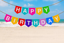 Hanging Multicolor Party Fags Banner With Happy Birthday Sign On A Sea Or Ocean Beach. 3d Rendering