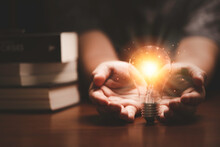 Businessman Holding Orange Light Glowing From Lightbulb Infant Of Heap Of Books For Study And Learning Can Make Creative Thinking Idea And Knowledge To Problem Solving Concept.