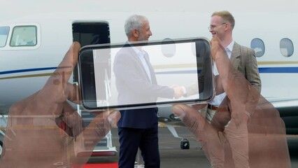 Canvas Print - Composite video of hand holding a smartphone over two businessmen shaking hands at the airport