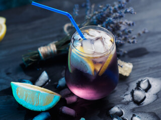 Wall Mural - a glass of lavender lemonade with lemon on a dark table. refreshing craft drink