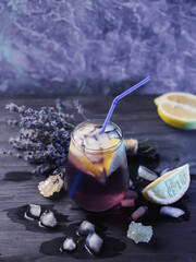 Wall Mural - a glass of lavender lemonade with lemon on a dark table. refreshing craft drink