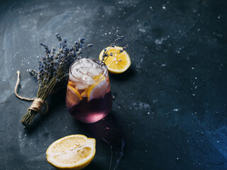 Wall Mural - a glass of lavender lemonade with lemon on a dark table. refreshing craft drink