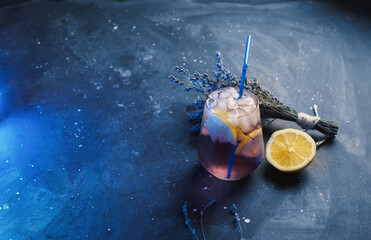 Wall Mural - a glass of lavender lemonade with lemon on a dark table. refreshing craft drink. blue backlight
