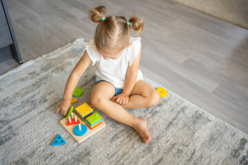 Wall Mural - Cute caucasian little girl playing on the floor at home with eco wooden toys. Montessori toy. The child playing educational games.