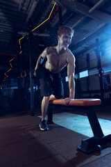 Wall Mural - Portrait of young shirtless muscular man training, doing exercises with dumbbells isolated over gym interior