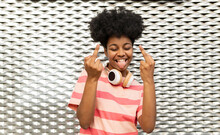 Happy Young Woman With Eyes Closed Gesturing Middle Fingers In Front Of Wall