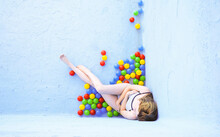 Woman With Multi Colored Plastic Balls Sitting By Blue Pool Wall