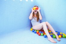 Happy Woman Covering Eyes With Balls Sitting In Front Of Blue Pool Wall