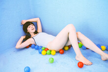 Woman Lying Amidst Multi Colored Balls By Blue Pool Wall