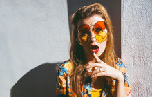Woman With Mouth Open Wearing Red And Yellow Sunglasses In Front Of Wall