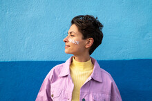 Woman With Peace Text On Cheek In Front Of Blue Wall
