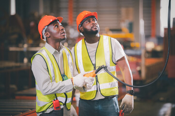 Team African American Black afro worker in factory, industrial engineer wearing helmet while standing in a heavy industrial factory behind. The Maintenance looking of working at industrial machinery