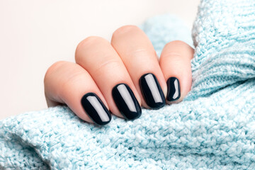 Wall Mural - Female hand in blue knitted sweater with beautiful manicure - dark black nails. Nail care concept