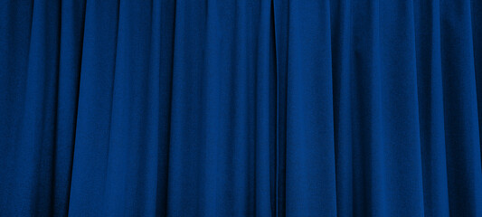 close up view of dark blue curtain in thin and thick vertical folds made of black out sackcloth fabric, panoramic view of drapery use as background. abstract theatre backgrounds and wallpapers.