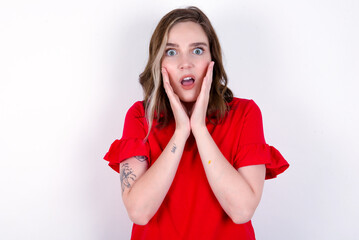 Upset young caucasian woman wearing red T-shirt over white background touching face with two hands