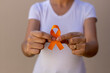 woman in white t-shirt holding orange ribbon. skin cancer prevention campaign