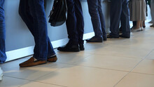 View Of Legs Of Customers Standing N The Modern Office, Getting Served In The Bank. Media. People Are Queuing For Service In The Department Of A Bank.