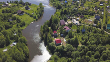 Aerial View Of A Town With Many Green Trees Located Along The River In A Sunny Summer Day. Clip. Ecologically Clean Area With Small Beautiful Houses And Narrow River.