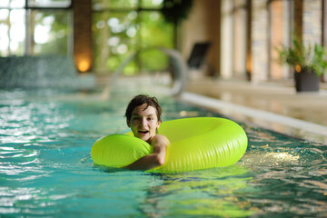 Wall Mural - Cute young girl playing with inflatable ring in indoor pool. Child learning to swim. Kid having fun with water toys. Family fun in a pool.