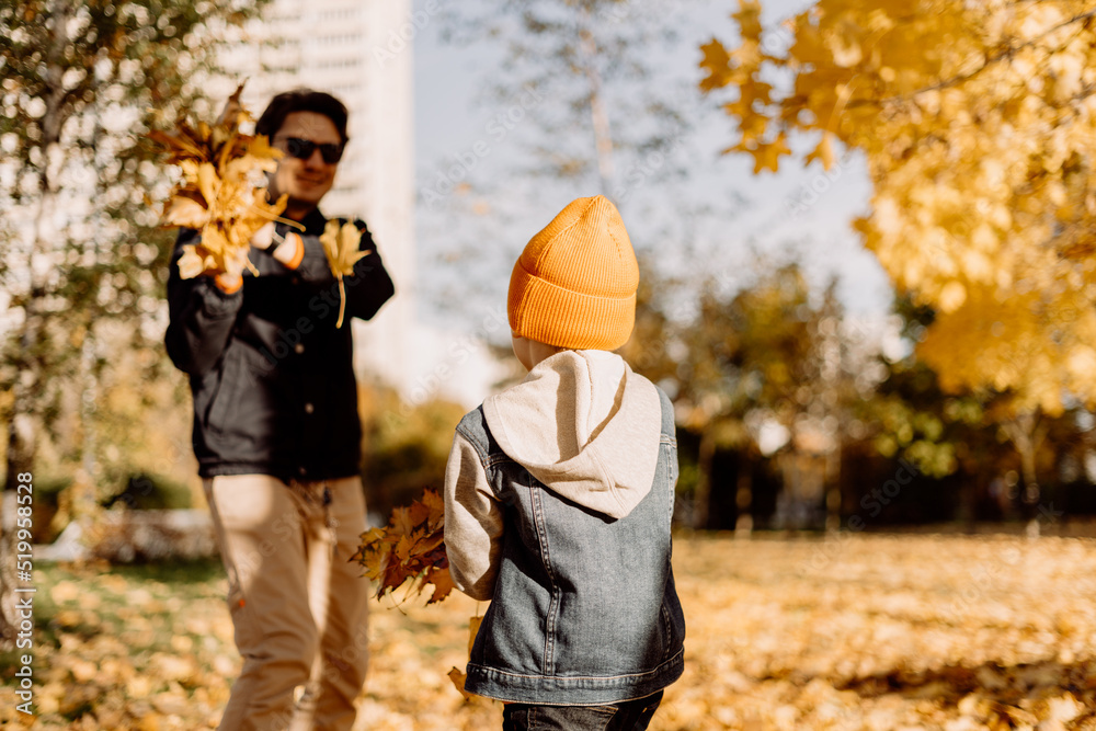 Father and son having fun in autumn park with fallen leaves, throwing ...