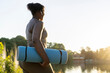 © gpointstudio - Plus sized African American woman walking with exercise mat and earphones through the park in a summer day