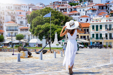 A tourist woman in a white summer dress explores the beautiful town of Skopelos island, Sporades, Greece