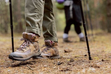 Close up of woman's rugged hiking boots and jeans on a leaf covered forest trail. Hiker in the middle of image with forest behind her.