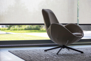 Leinwandbilder - Roller blinds of large sizes on the window in the interior. Automatic solar shades, fabric with linen texture. In front of a large window is a chair on a carpet. Outside is a view of the garden.