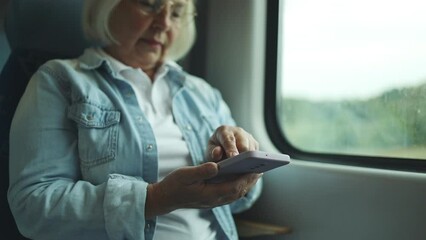 Wall Mural - Senior woman in glasses looking at screen mobile phone near big windows, traveling by train in Europe