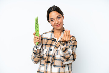 Poster - Young hispanic woman holding a green beans isolated on white background inviting to come with hand. Happy that you came