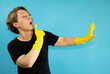 Adult cleaning woman in a black T-shirt on a blue isolated background. A woman shows her hands on a blue background in yellow gloves for cleaning