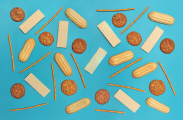 different types of dessert cookies, waffles and straws isolated on blue background. Top view, flat lay.