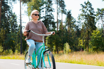 Senior older elderly modern woman rides a bicycle in a city park in the forest. Active pensioner, health lifestyle