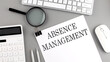 ABSENCE management written on paper with office tools and keyboard on the grey background