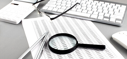 Poster - Office desk workplace with keyboard, charts and magnifier on grey table. Top view with