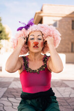 Middle Aged Female Clown Putting On Red Nose On City Street