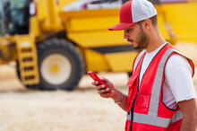 Concentrated Man Browsing Smartphone Near Combine Harvester