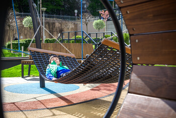 Wall Mural - Cute little blond caucasian boy relaxing and having fun in multicolored hammock in backyard or outdoor playground. Summer active leisure for kids. Child swinging on hammock. Activities for children