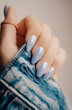 Beautiful blue nail manicure. Stylish pastel blue manicure. Nail polish. Female hands manicure close up view on blue denim jacket background.